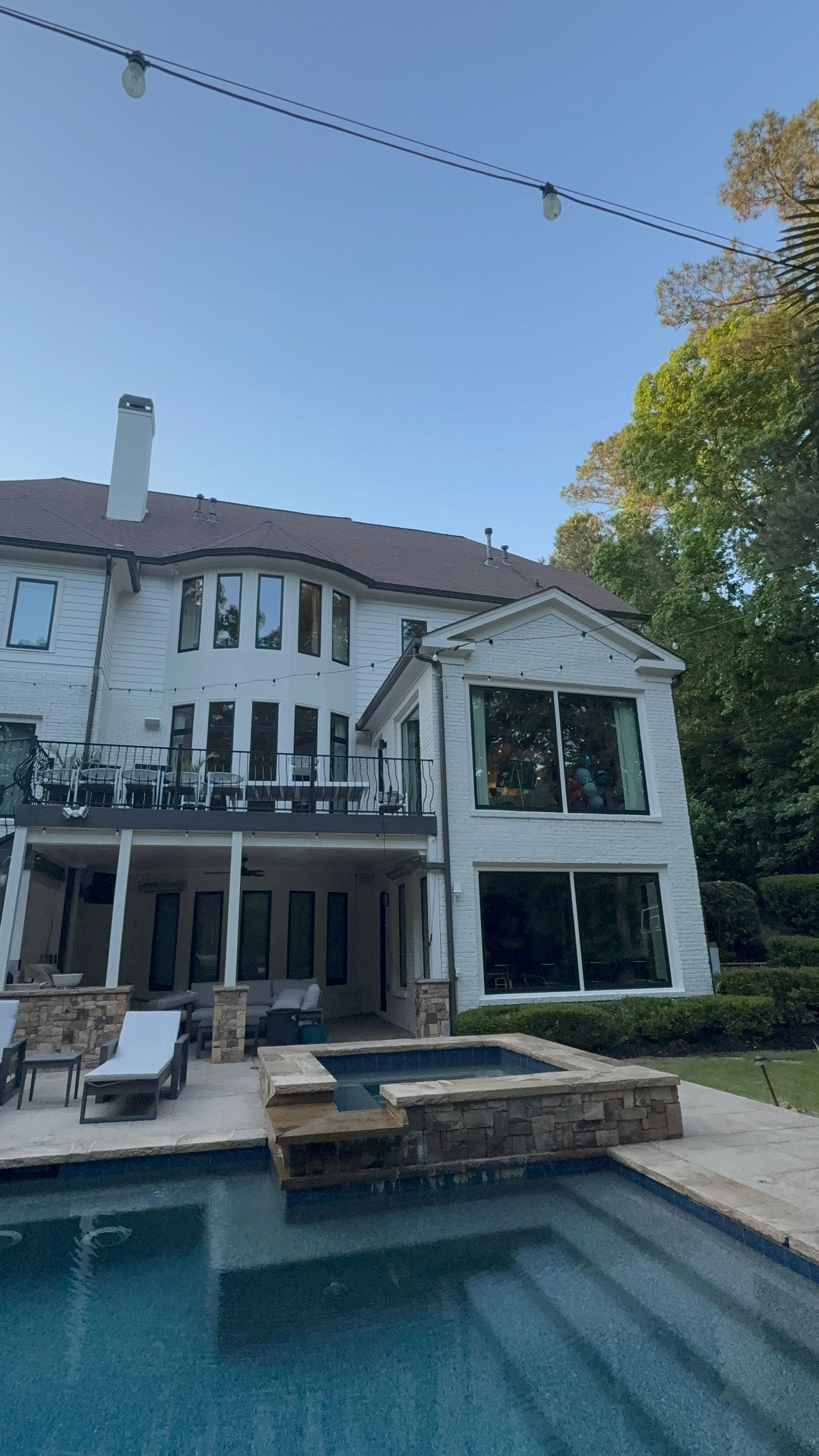 Modern white house with large windows and a backyard pool under a clear blue sky