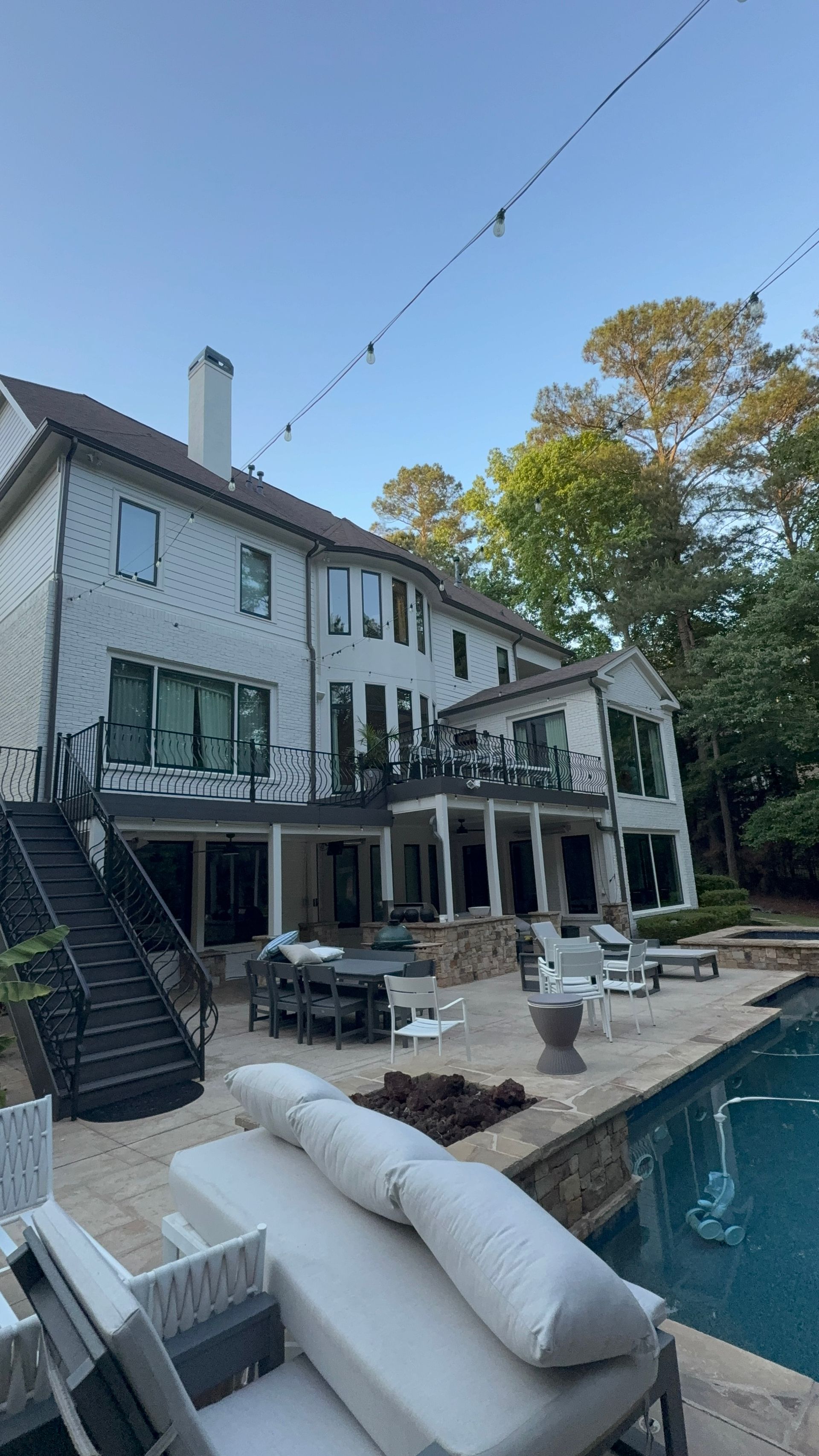 Backyard patio with white house, pool, and outdoor seating beside a deck and staircase