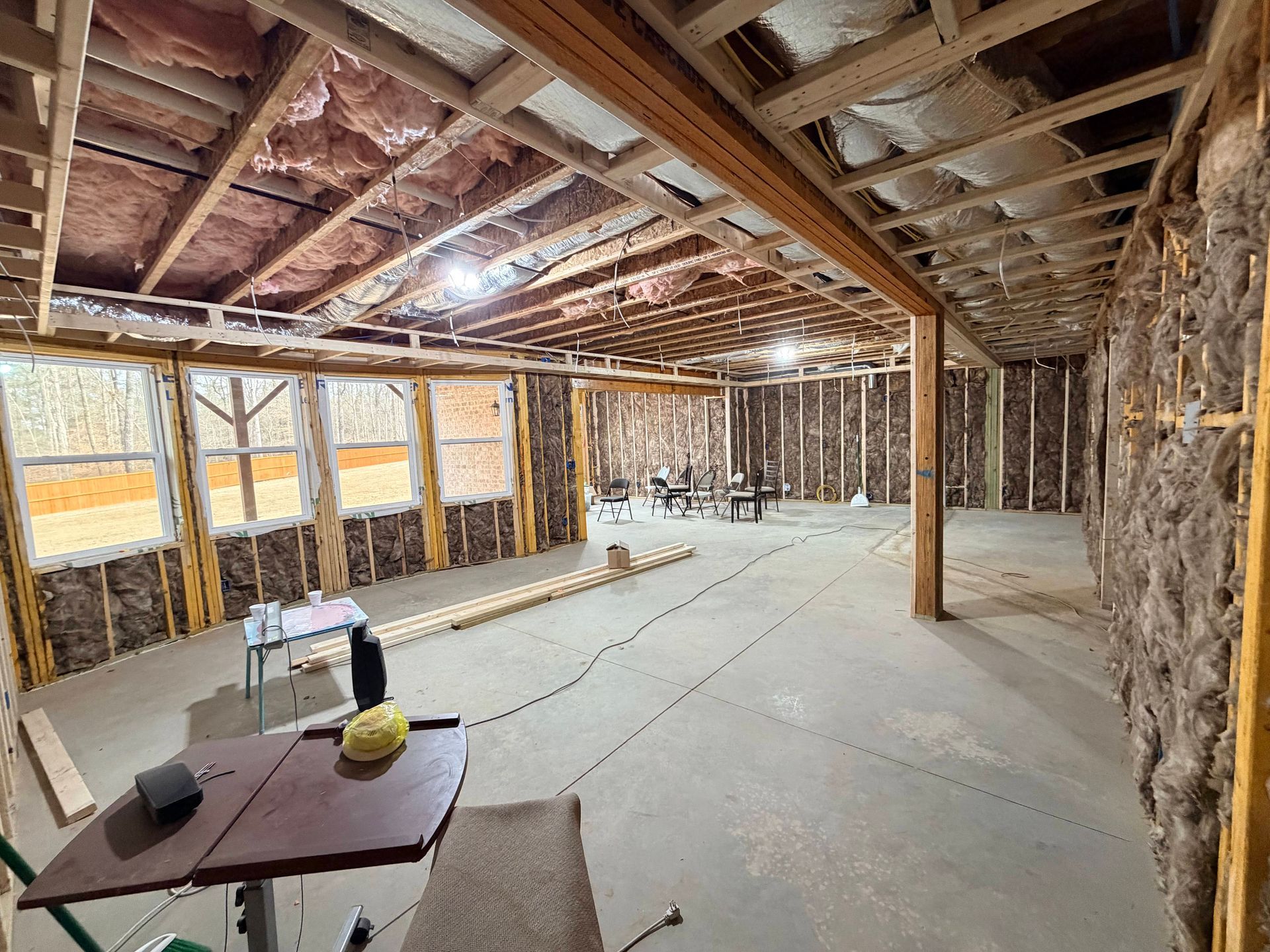 Unfinished basement with exposed studs and insulation, concrete floor, and a small table in the foreground