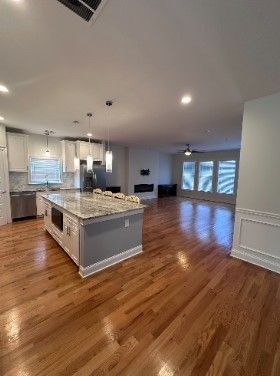 Bright open kitchen and living area with hardwood floors, island, pendant lights, and large windows