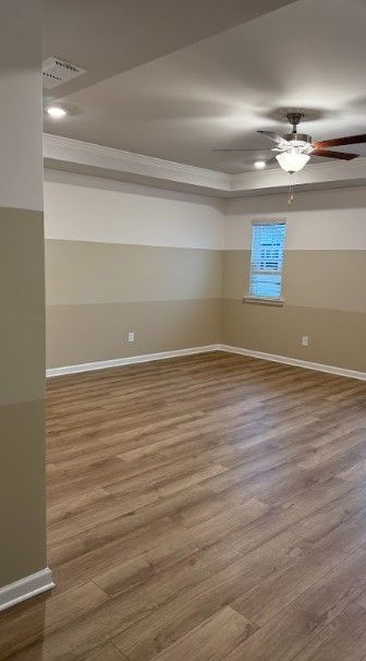 Empty beige room with wood-look floors, tray ceiling, ceiling fan, and a small window.