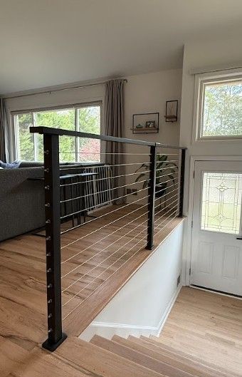 Indoor staircase with black railings and wire balusters beside large windows and a white door