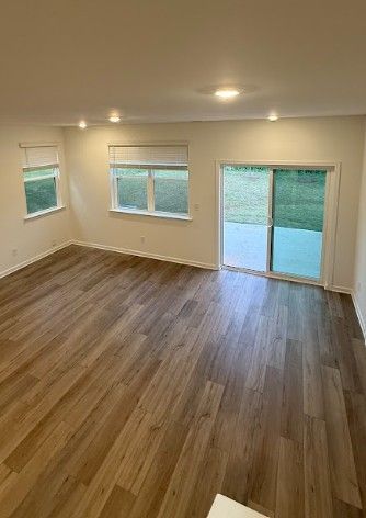 Empty living room with wood floors, beige walls, recessed lights, and large windows by a sliding glass door