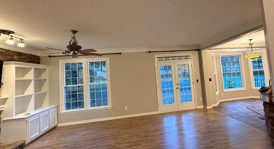 Empty living room with built-in shelves, hardwood floors, ceiling fan, and French doors to a deck.