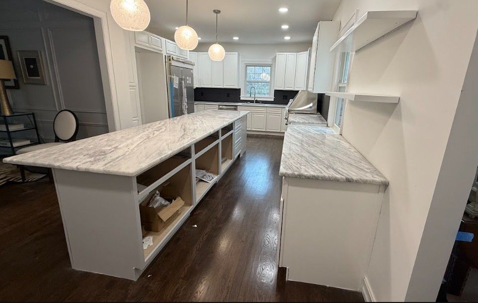 Bright modern kitchen with marble island, white cabinets, pendant lights, and dark wood floors