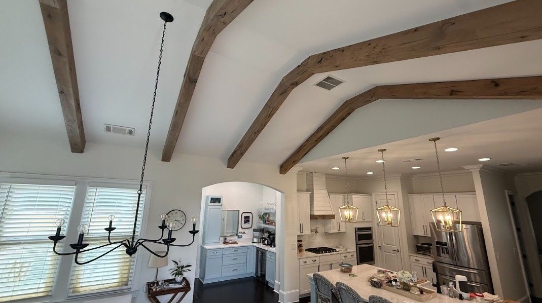 Bright kitchen and dining area with exposed wooden ceiling beams, chandelier, and white cabinetry