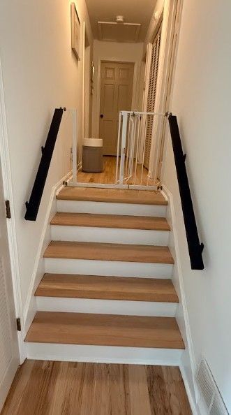 Narrow indoor staircase with wooden steps, black handrails, and a safety gate at the top landing