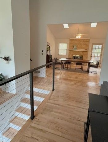 Modern home interior with wood floors, black railing, and dining area with fireplace and windows.