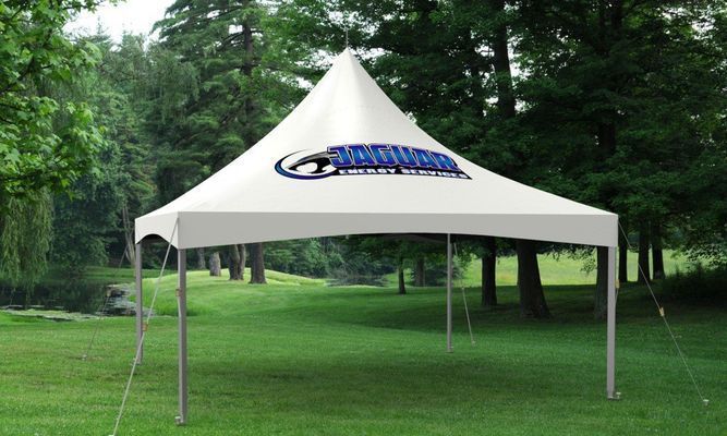 White tent with logo set up in grassy park with trees