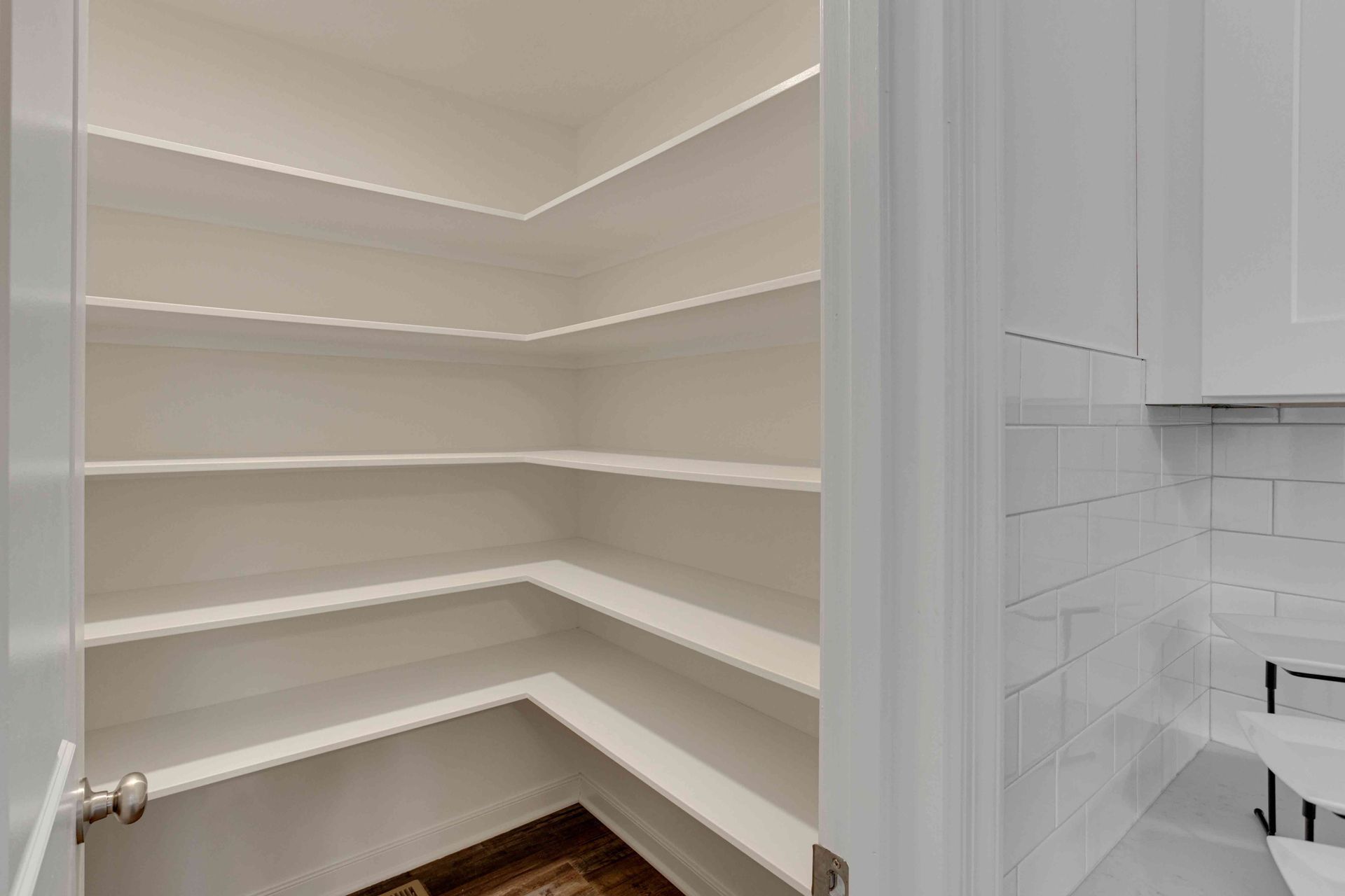 Empty white pantry with wraparound shelves beside a tiled bathroom vanity
