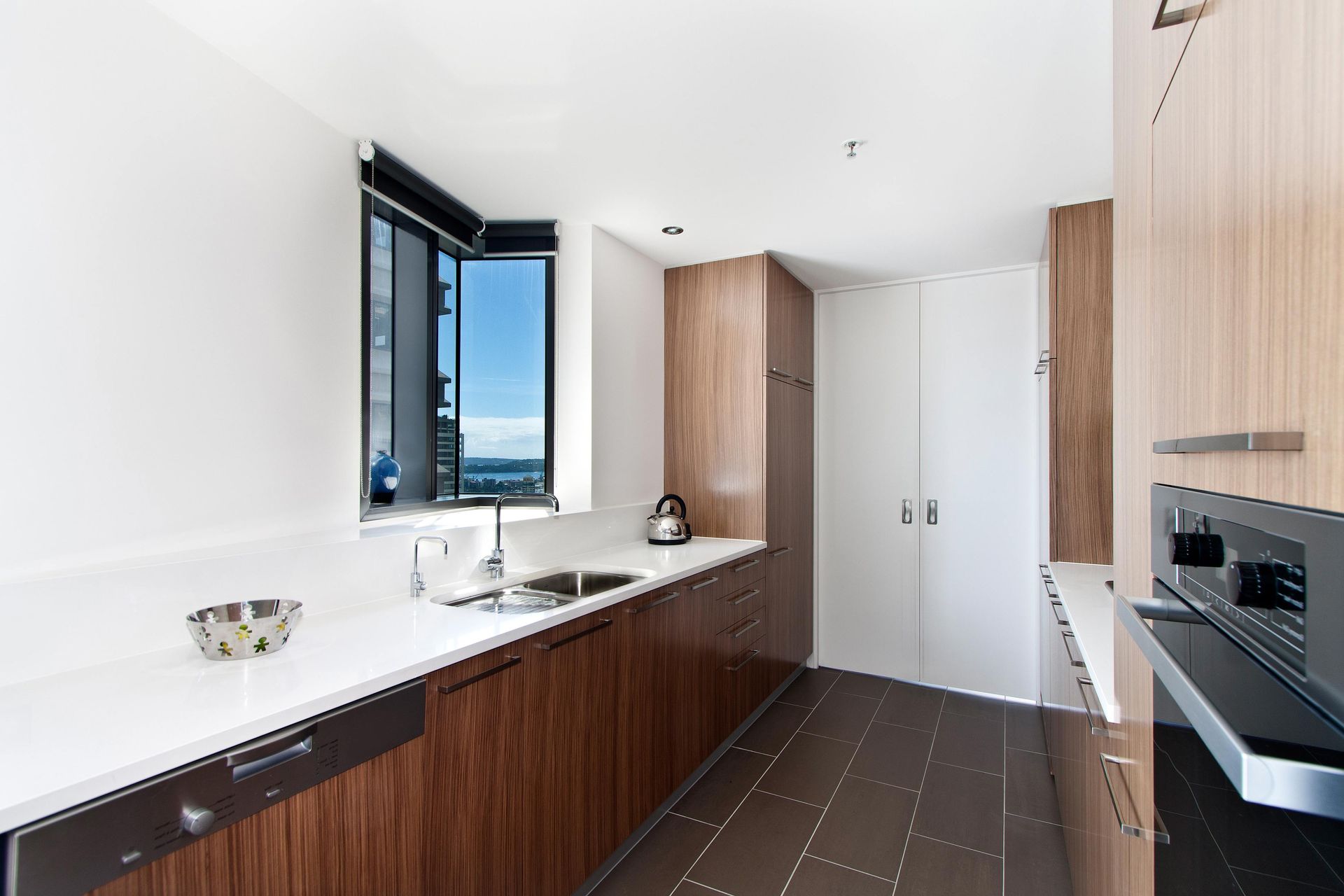 Modern kitchen with dark wood cabinets, white countertops, black tile floor, and an open window.