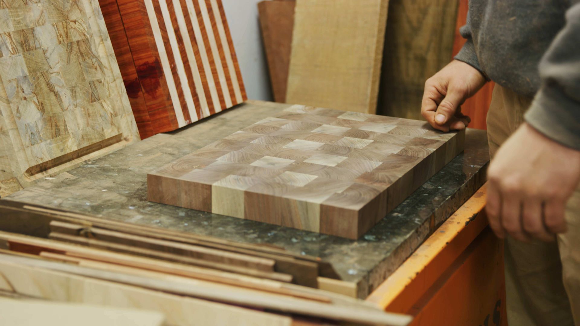 Woodworker holding a large wooden cutting board on a workbench in a workshop