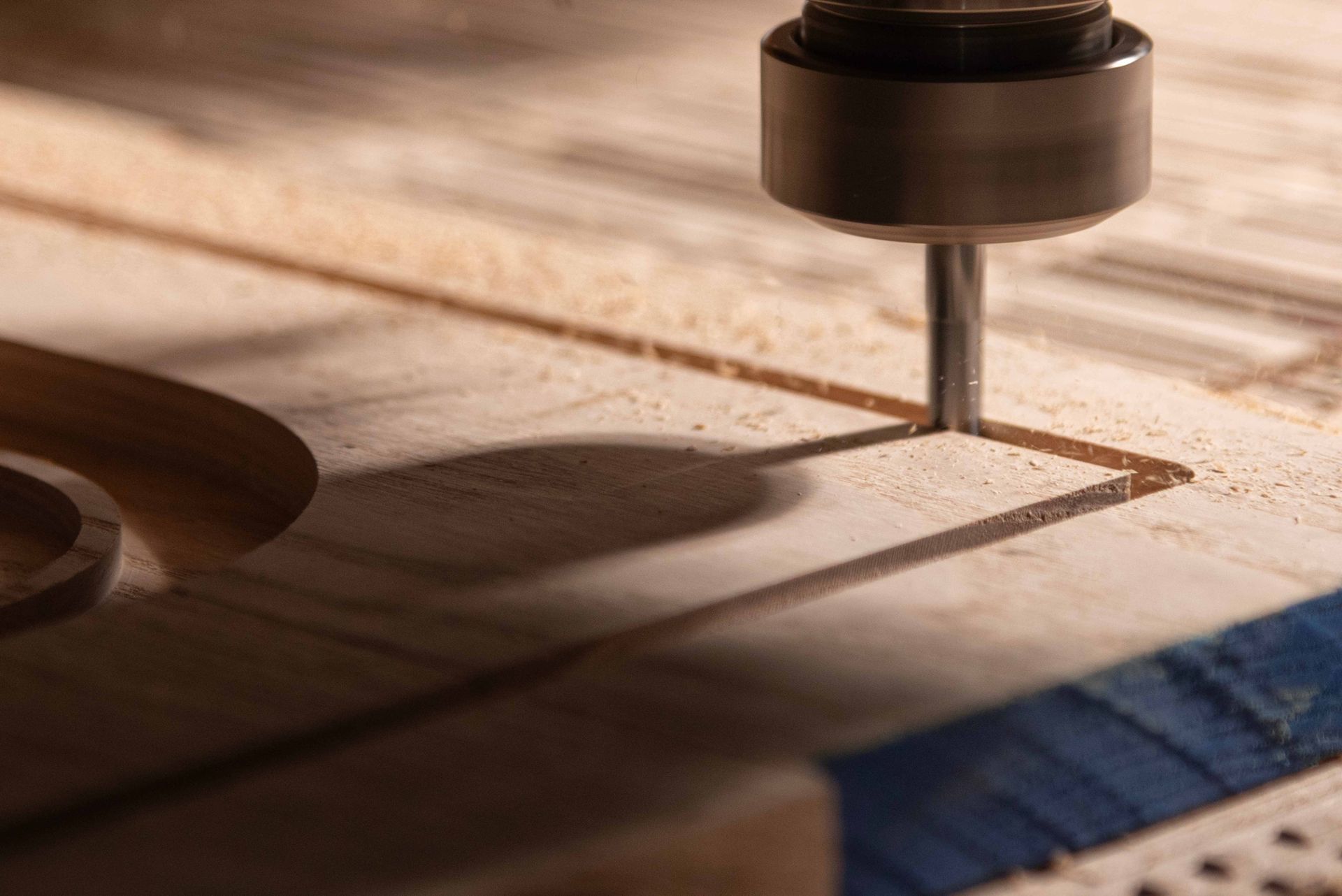 CNC router carving a wooden board, with sawdust and a blue tape measure nearby