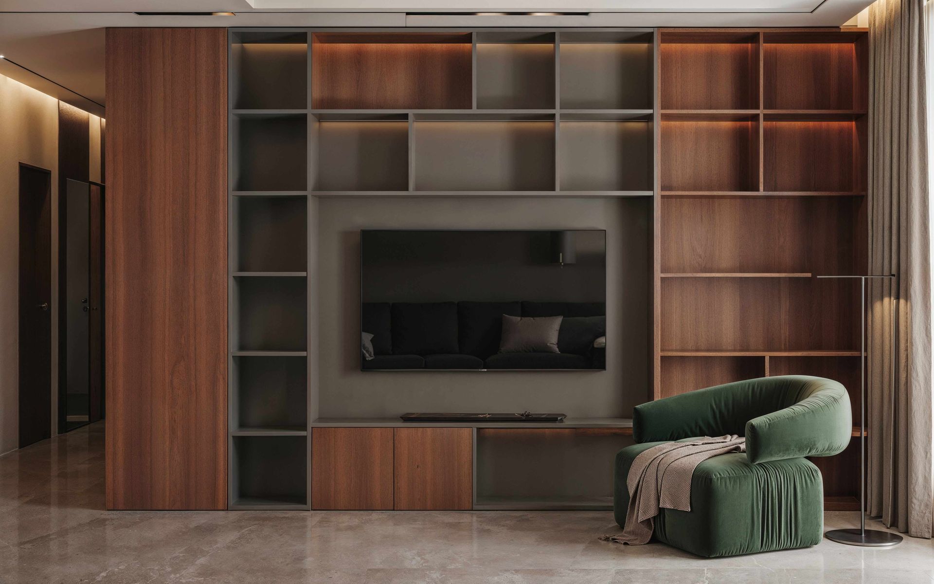 Modern living room wall unit with built-in shelves, TV, warm wood paneling, and a green armchair with blanket.