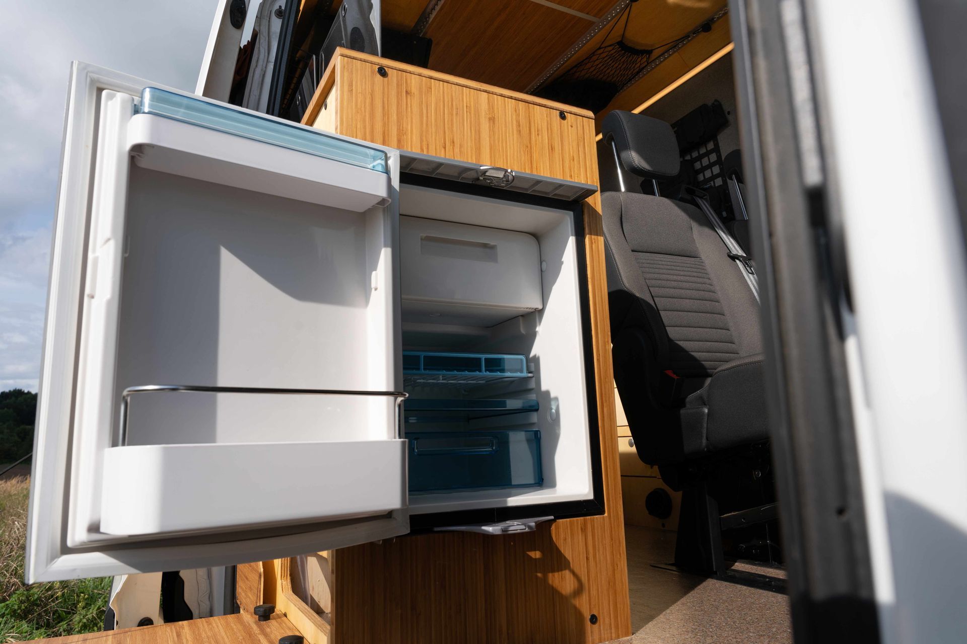 Open fridge beside a wooden post, showing shelves and bins in a garage or workshop.