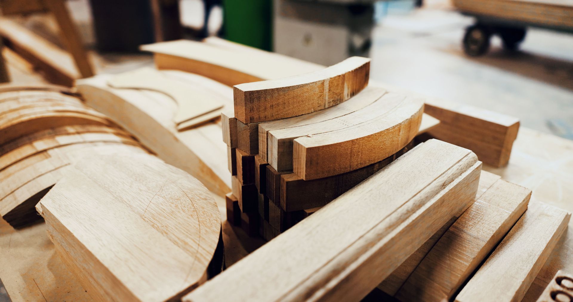 Stacked curved wooden boards in a workshop, showing layered light and dark wood pieces.