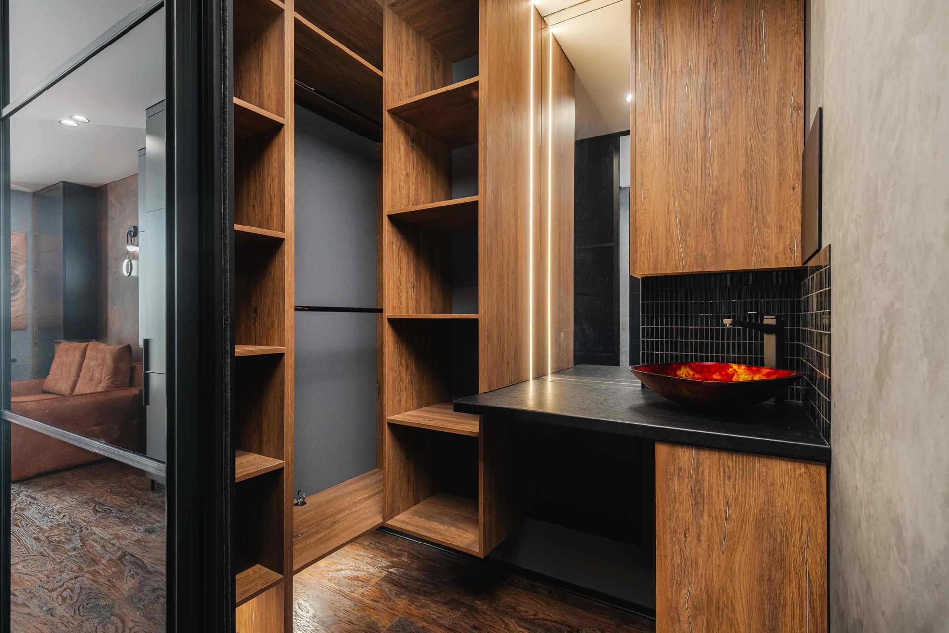 Modern kitchenette with wood cabinetry, black counters, open shelving, and a red bowl on the stove.