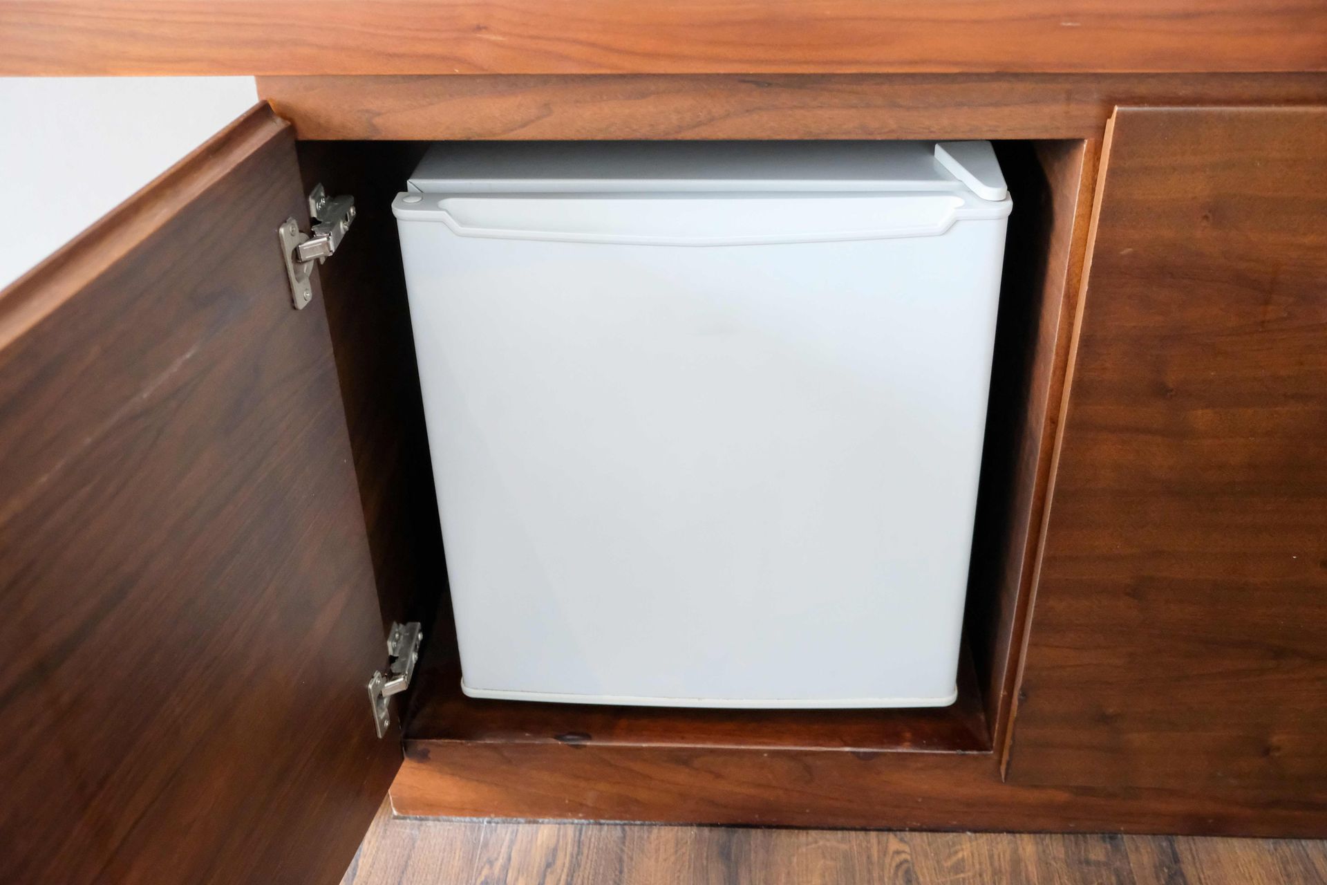 Small white mini fridge inside a wooden cabinet with the door open