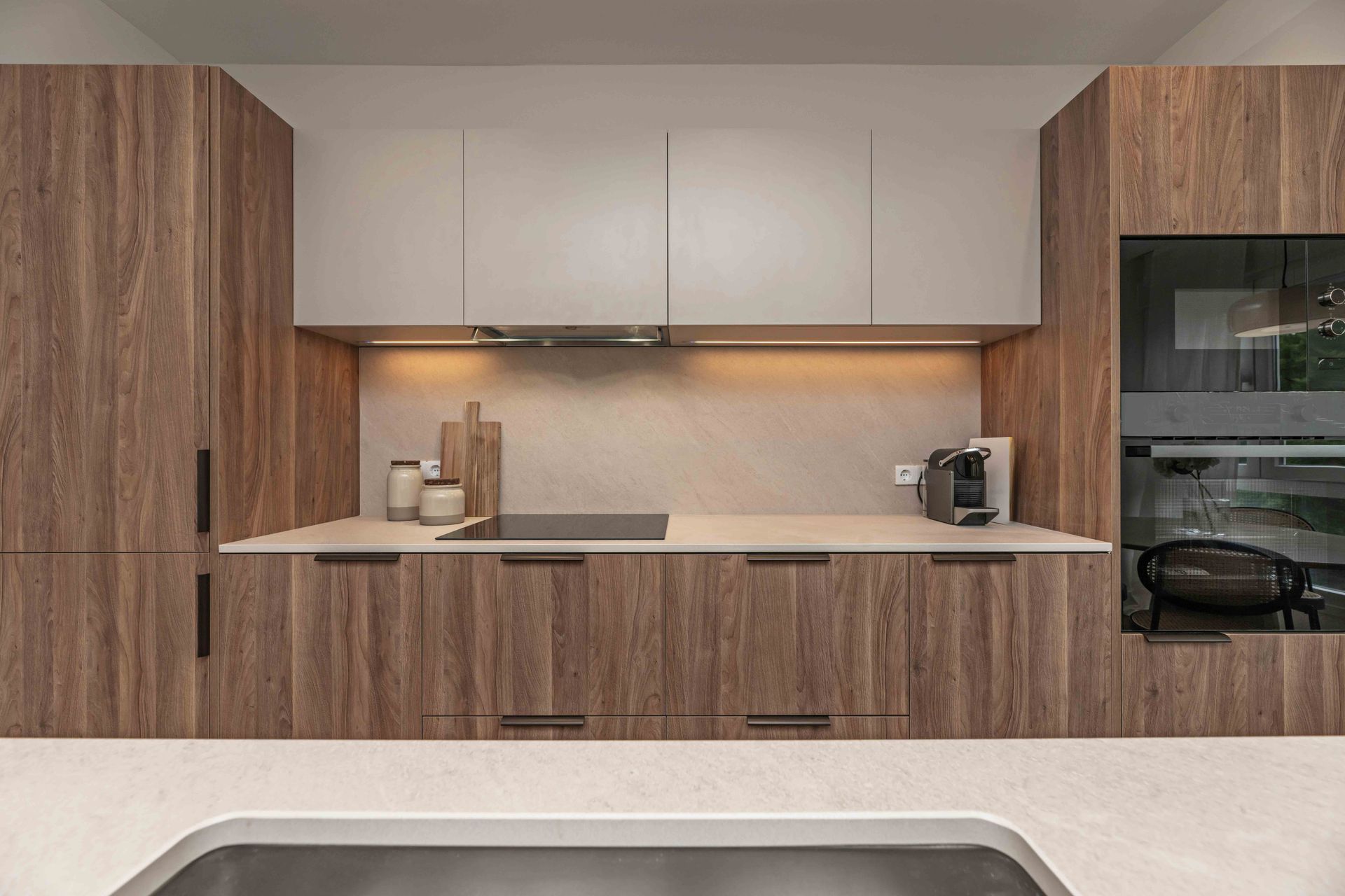 Modern kitchen with wood cabinetry, white upper cabinets, and a built-in oven on the right.