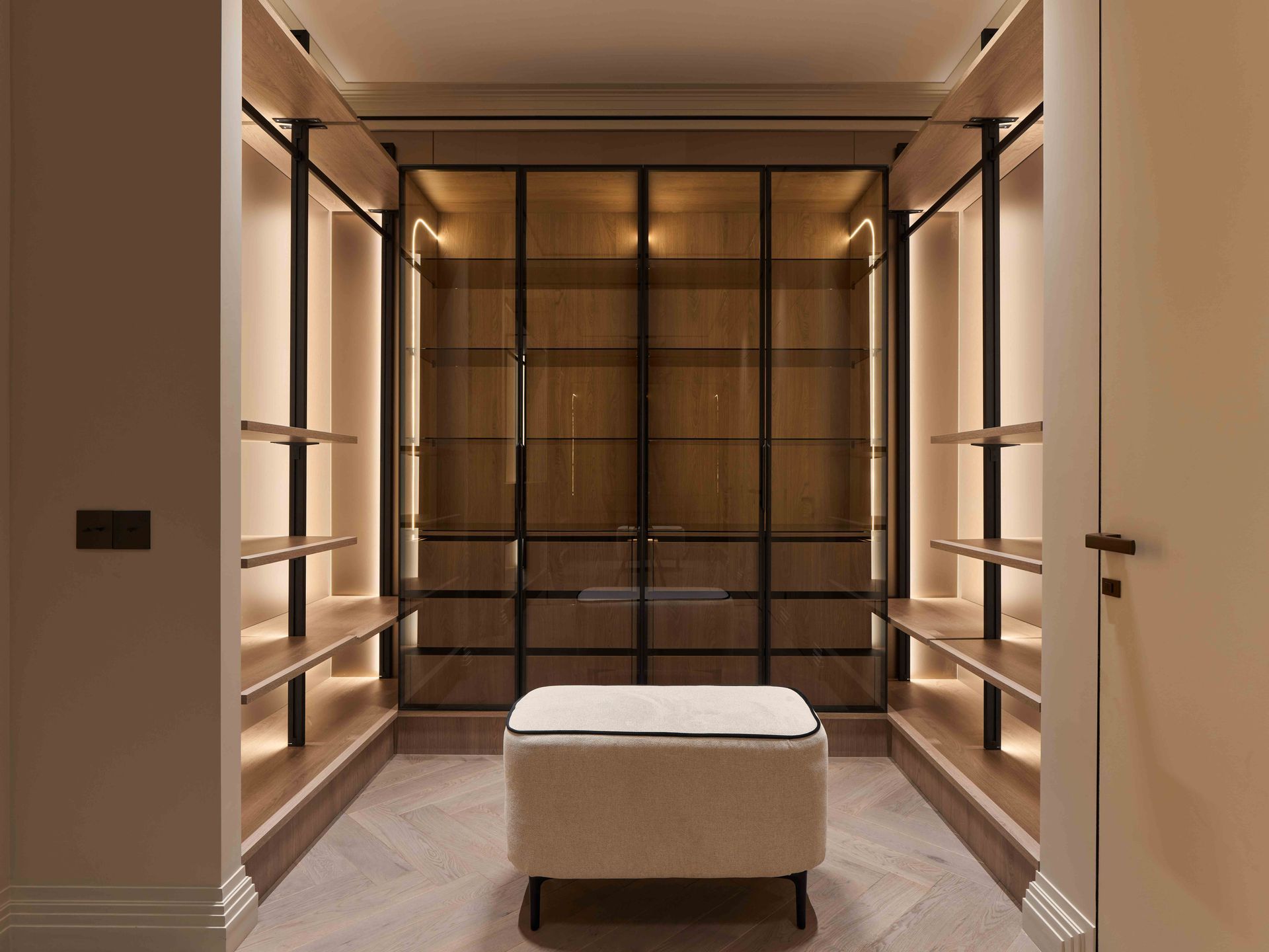 Luxury walk-in closet with built-in shelves, glass doors, and a central upholstered bench.