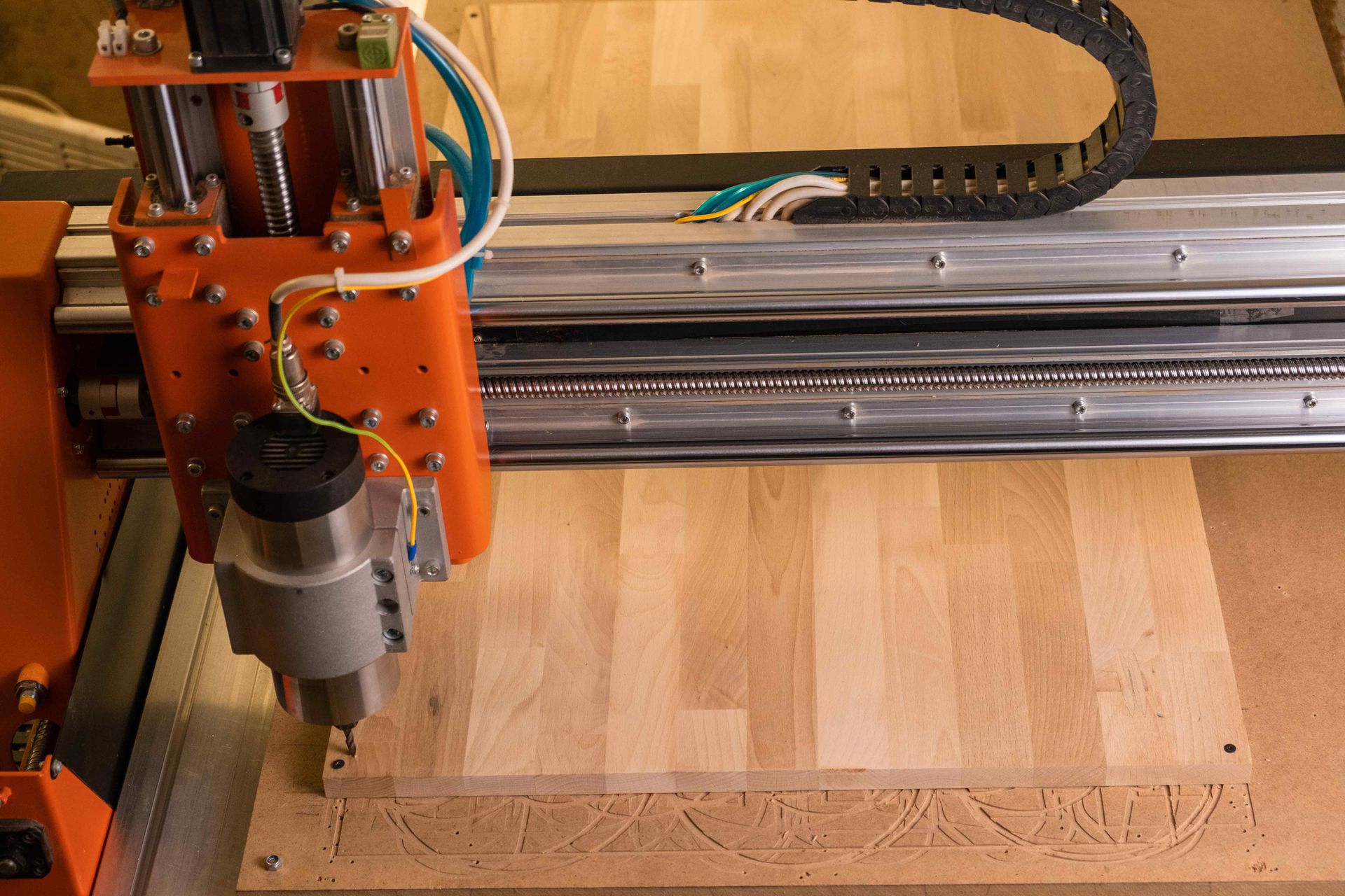 CNC router carving wood on a workbench with orange machine parts and silver rails