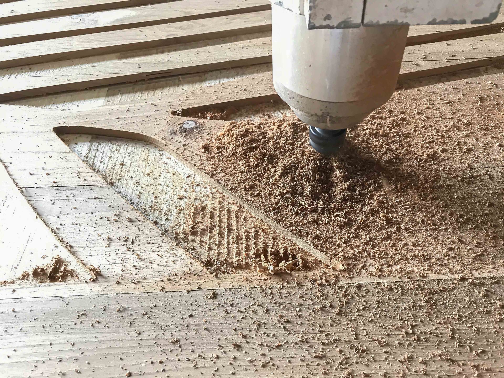 CNC router carving a wood panel, with sawdust scattered across the work surface