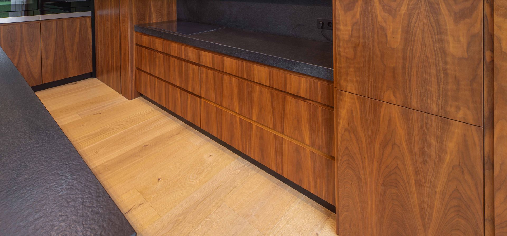 Wood-paneled bench with black cushion beside a gray carpet and light wood floor in a hallway