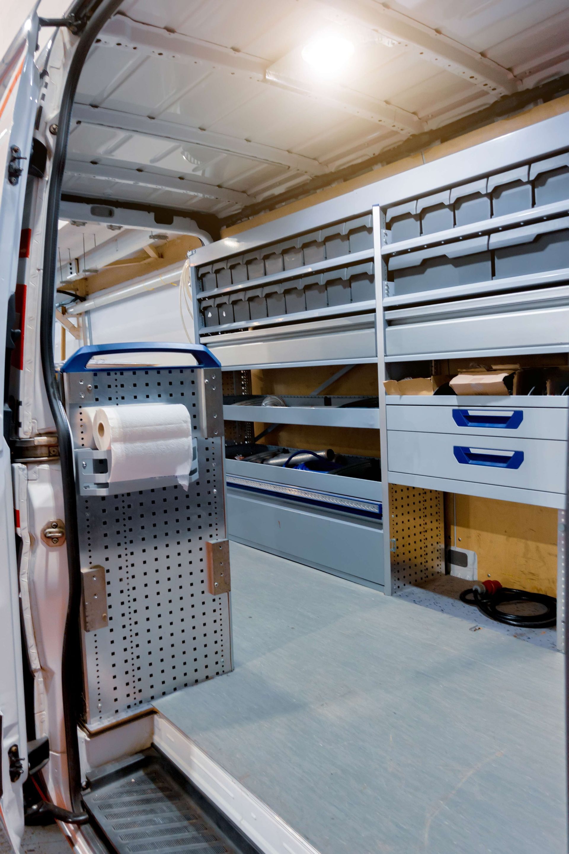 Cargo van interior with shelving, storage bins, and a workbench on the left wall