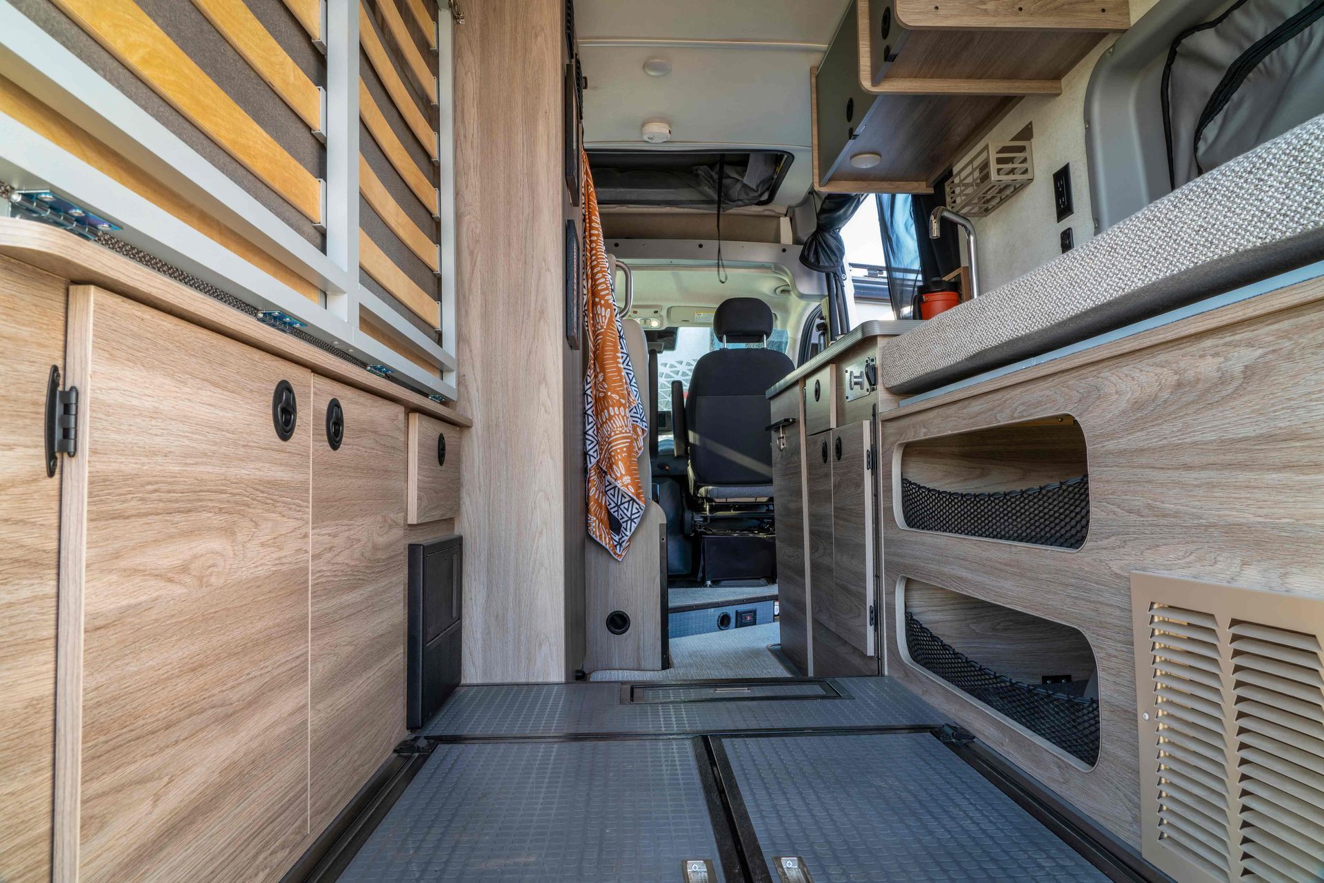 Interior of a camper van aisle with wood cabinets, bench seating, and a front driver’s seat visible
