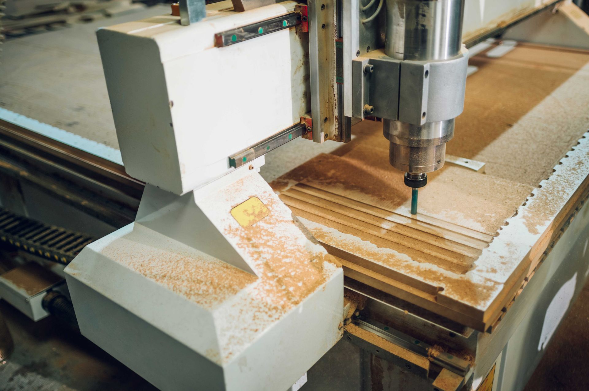 CNC router carving a wooden board, with wood shavings on the machine bed.