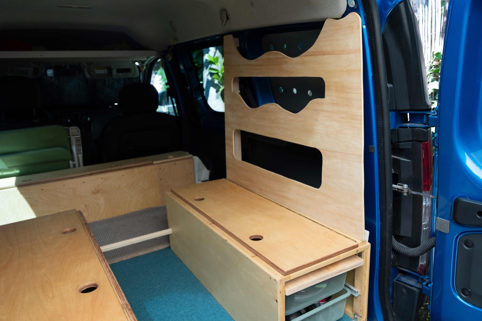 Blue van interior with folded wooden camper bed and storage cabinets