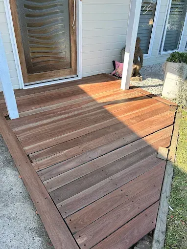 Wooden deck ramp with railings leading to a house entrance, lit by sunlight