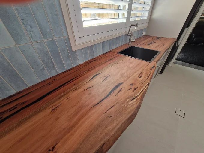Wooden kitchen countertop with black sink under a window, set against blue tile backsplash.