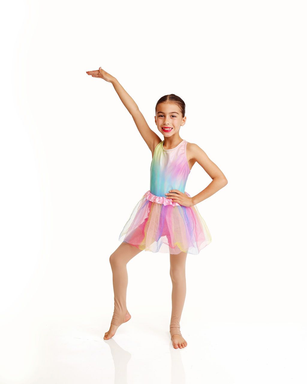 Young dancer in a pastel rainbow tutu poses with one arm raised and one hand on hip against a white background