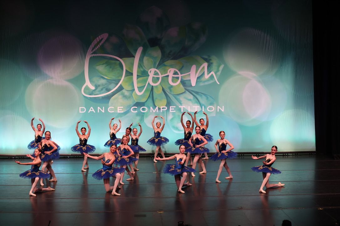 Dance troupe in blue costumes performing onstage under a Bloom Dance Competition backdrop