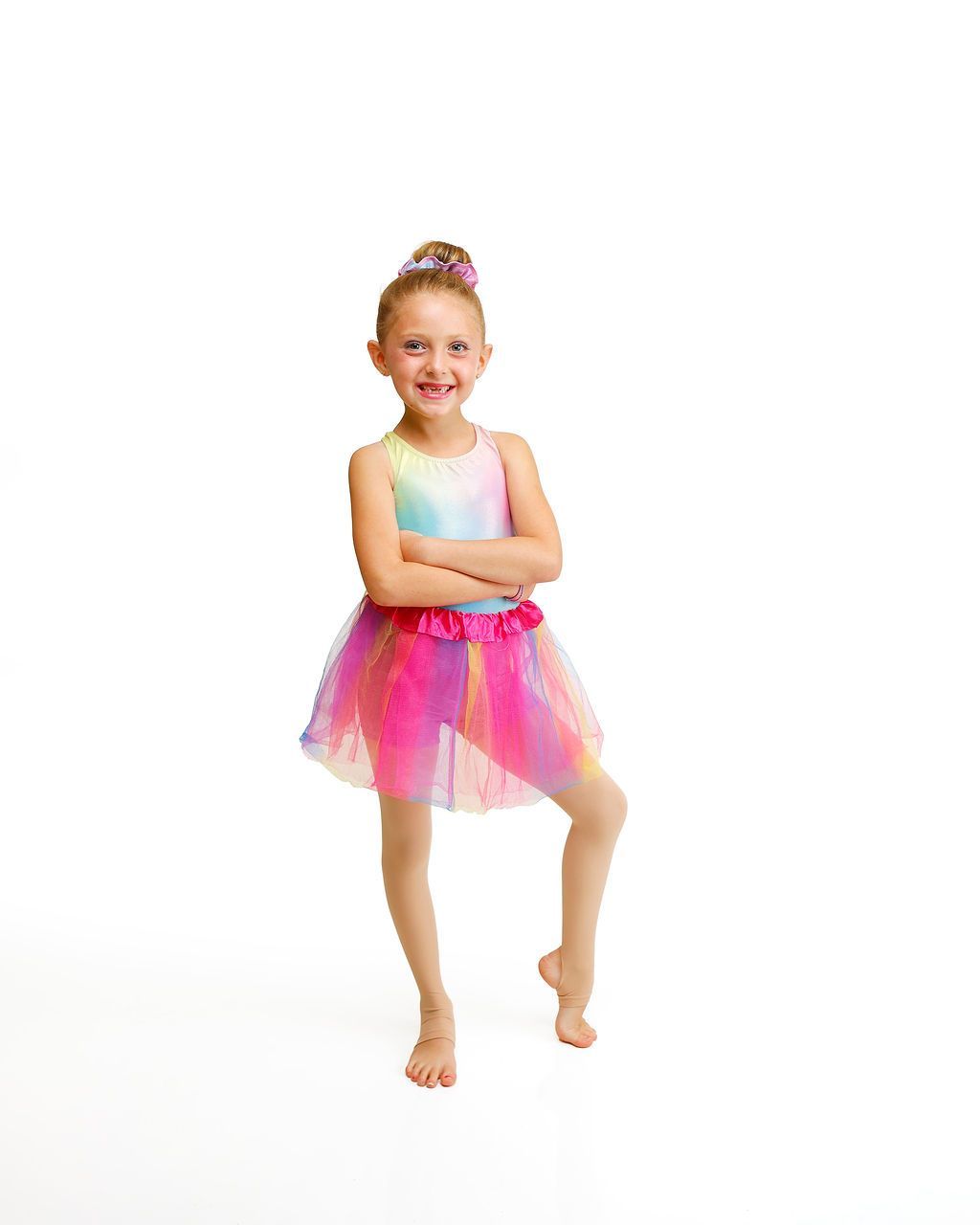 Young dancer in a rainbow tutu standing on one leg against a white background