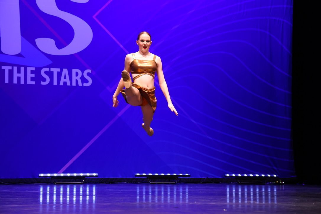 Dancer mid-leap on a purple-lit stage with “THE STARS” in the background