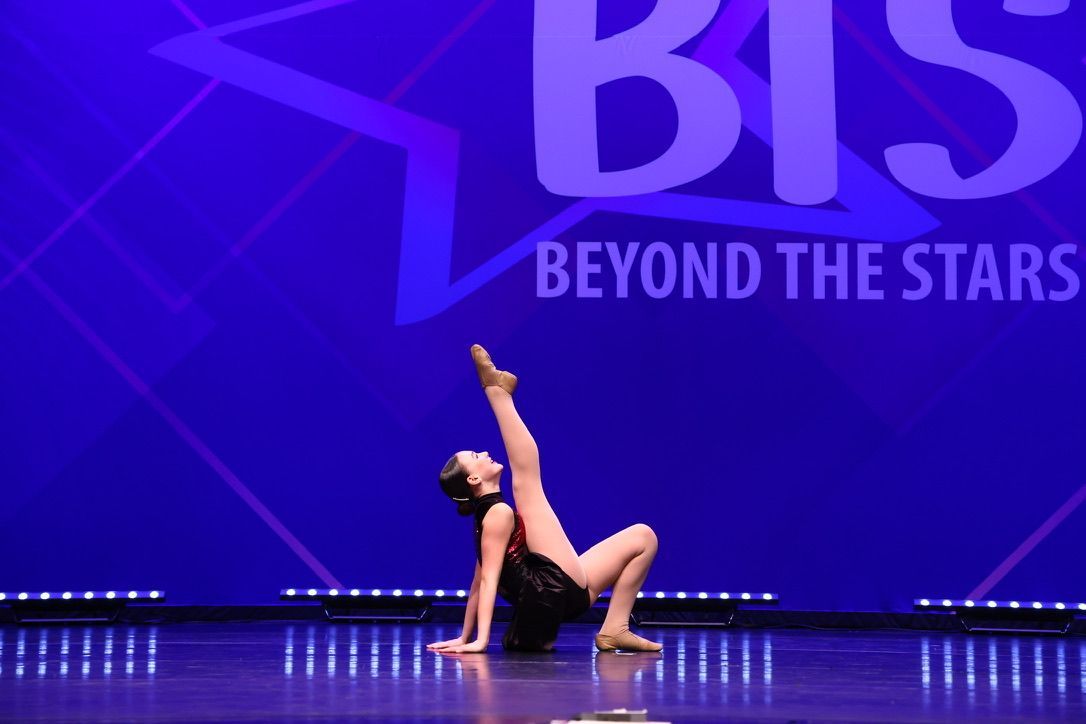 Dancer on stage in a purple-lit BIS Beyond the Stars performance, posing in a dramatic backbend.