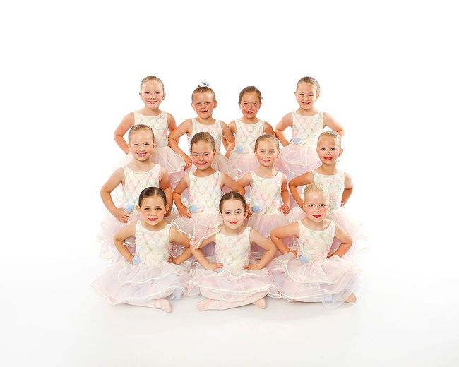 Group of young ballet dancers in white tutus posing in a studio
