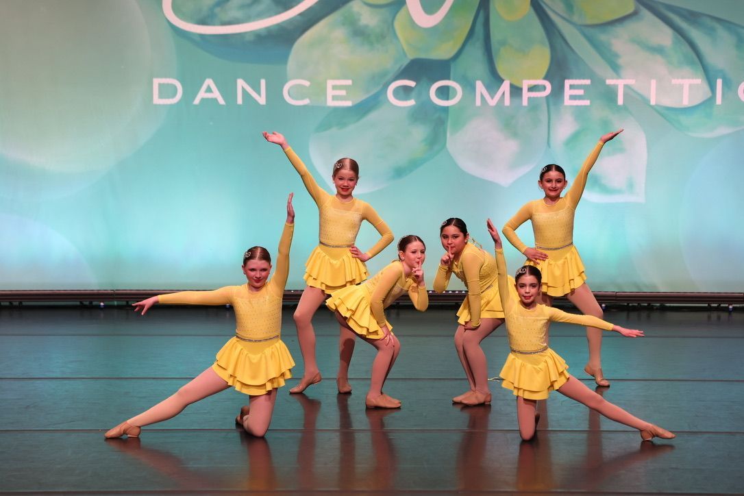 Five dancers in yellow costumes performing on a stage during a dance competition