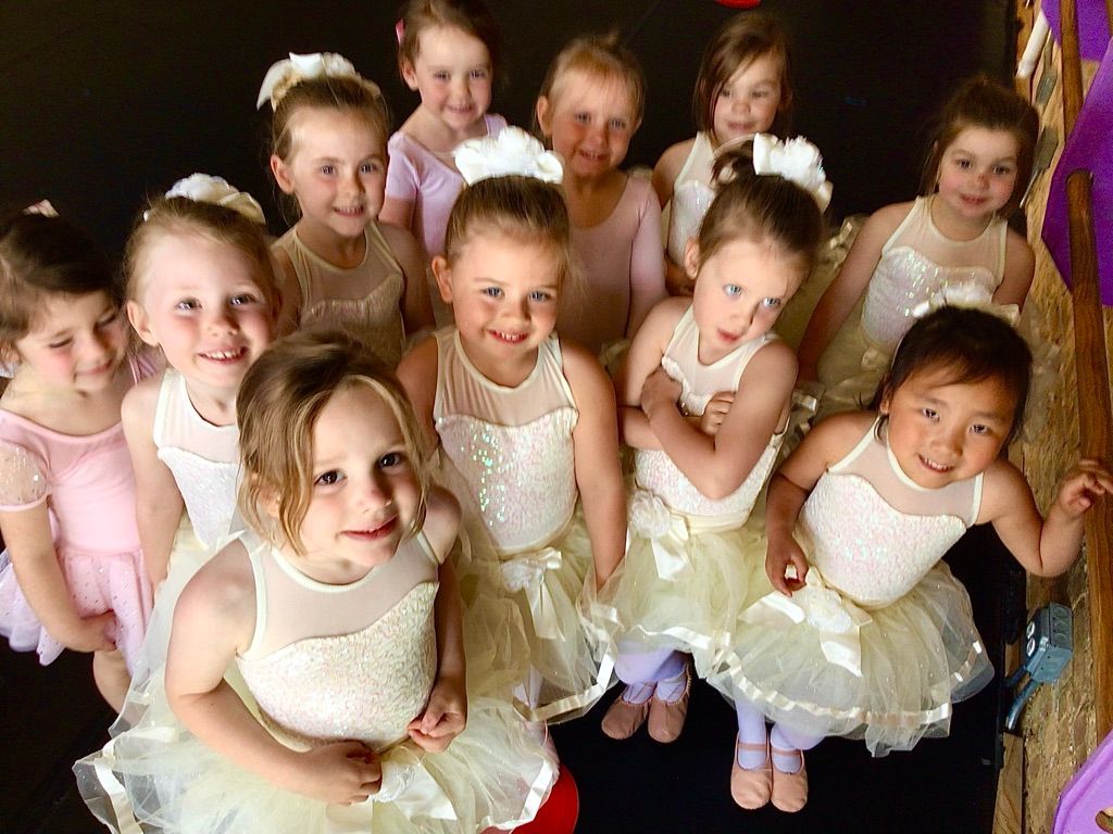 Group of children in pale dance costumes smiling and posing together indoors