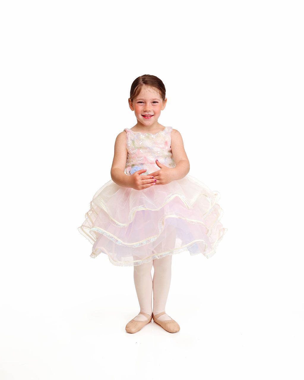 Young child in a pale pink ballet dress and tights standing against a white background.