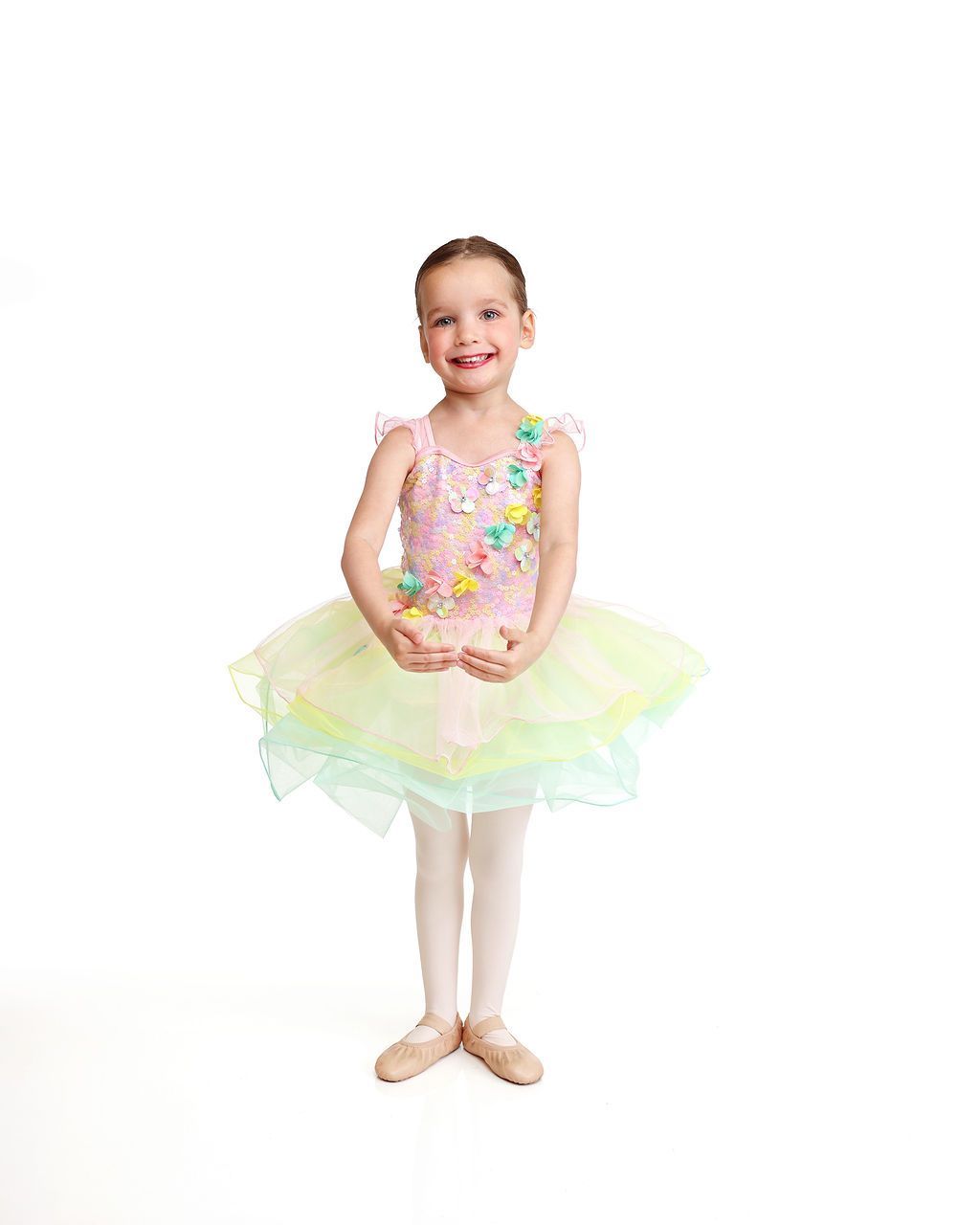 Child in a pastel tutu and sequined top, standing and smiling on a white background.