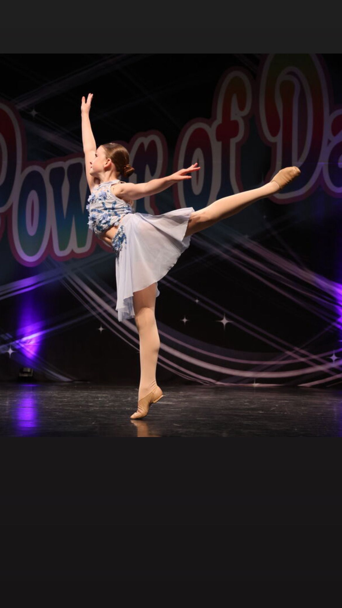 Dancer in a white costume striking a ballet pose onstage with a purple-lit backdrop