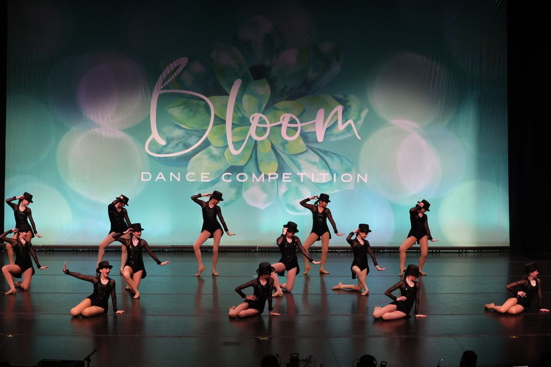 Dance troupe performing on a stage with teal lighting and a “Bloom” backdrop