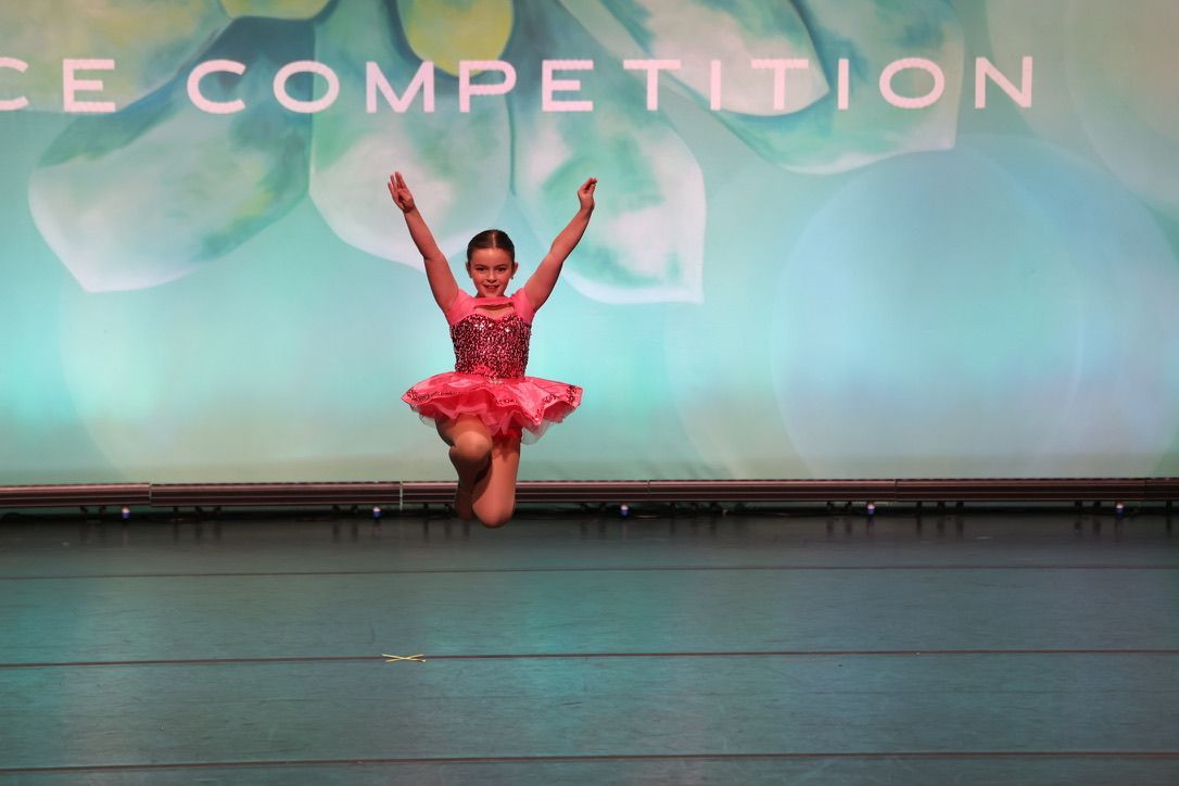 Young dancer in red costume leaps on stage under colorful competition backdrop