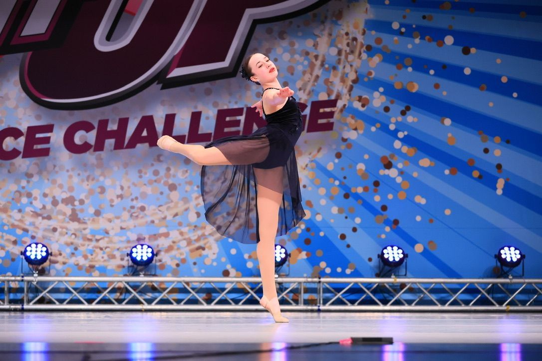 Ballerina in black costume posing on stage in front of a dance challenge backdrop