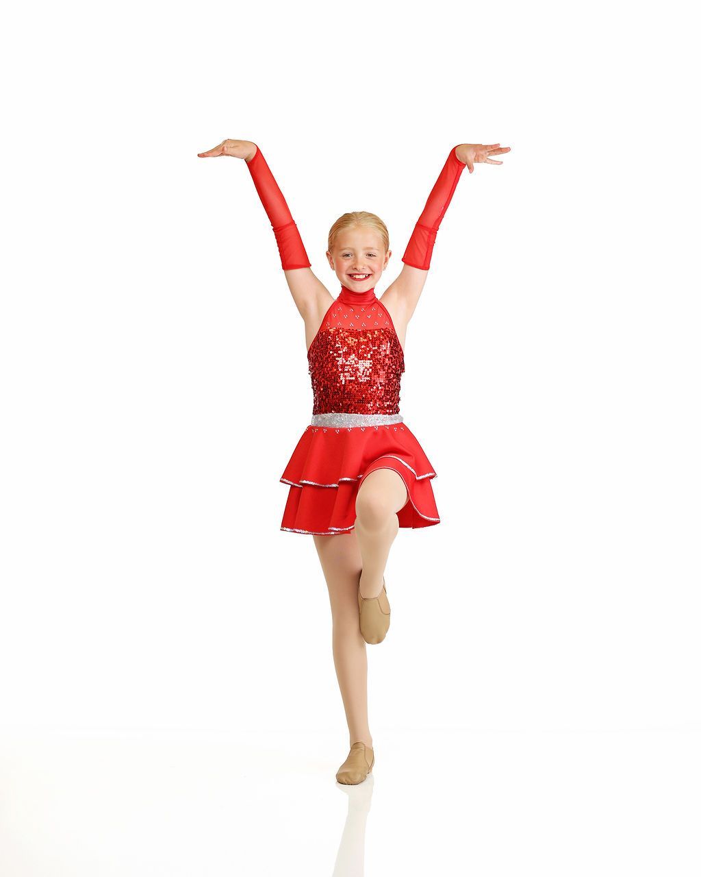 Young dancer in a red costume posing with arms raised and one leg lifted against a white background