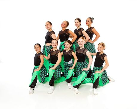 Group of dancers in black tops and green skirts posing in a studio on a white background
