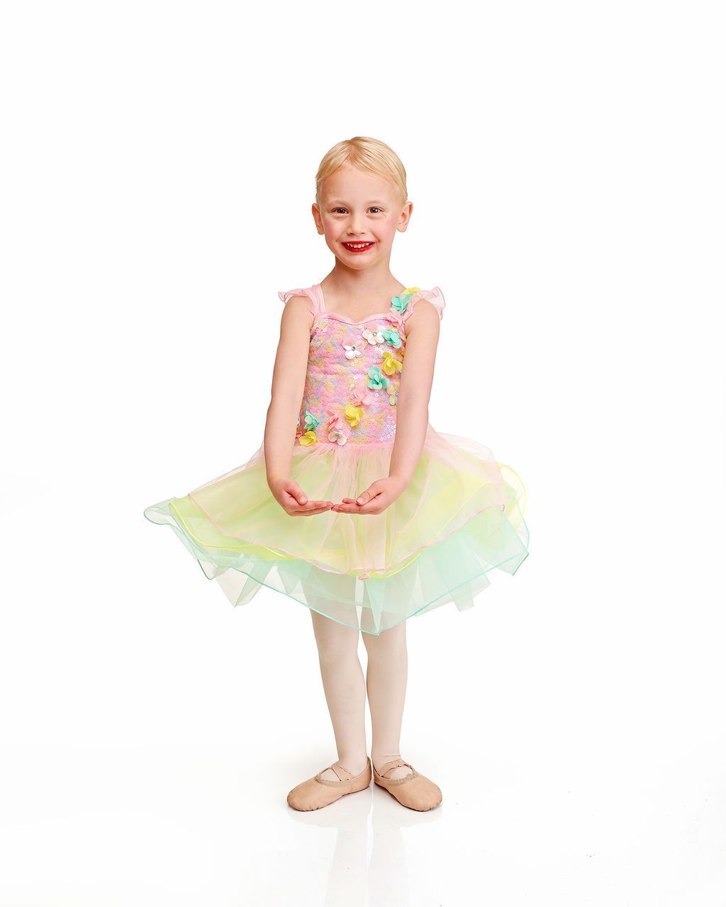 Young ballet dancer in a pastel tutu, standing on a white background and smiling